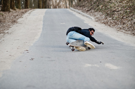 Fail falling from a skateboard. Street style arab man in eyeglasses with longboard longboarding down the road.の写真素材