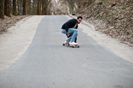 Street style arab man in eyeglasses with longboard longboarding down the road.の写真素材
