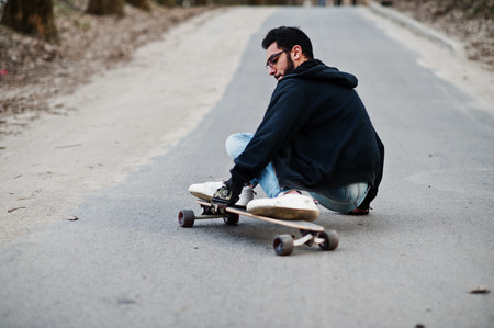 Street style arab man in eyeglasses with longboard longboarding down the road.の写真素材