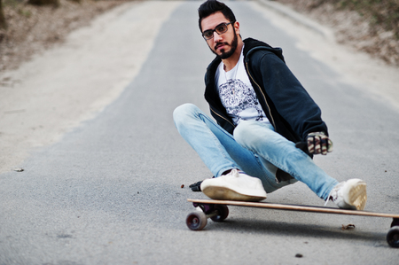 Street style arab man in eyeglasses with longboard longboarding down the road.の写真素材