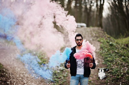Street style arab man in eyeglasses hold hand flare with red and blue smoke grenade bomb.の写真素材