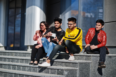 Group of asian people friends sitting on stairs outdoor against modern building and making selfie by phone.の写真素材