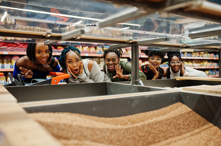 Group of five fun african womans with shopping carts choose buckwheat groats in supermarket.