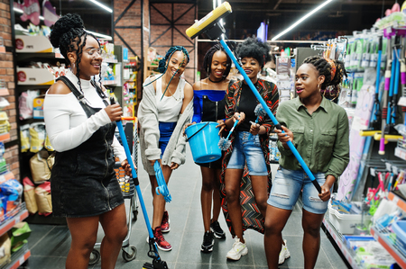 Group of five african womans with dust mop, toilet brush and bucket having fun in household cleaning items department in supermarket.の写真素材