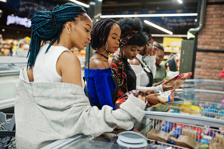 Group of african womans with shopping carts near refrigerator choose packs of dumplings in the supermarket.の写真素材