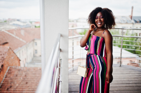 Fashionable african american woman in pink striped jumpsuit, with handbag posed in the french balcony.の写真素材