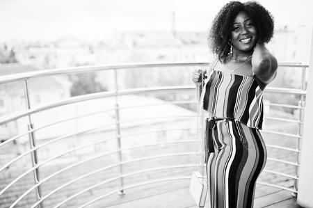 Fashionable african american woman in pink striped jumpsuit, with handbag posed in the french balcony.の写真素材