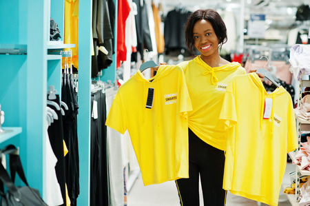 Afican american woman in tracksuits and sunglasses shopping at sportswear mall against shelves. She...