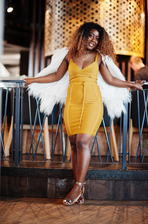 Glamour african american woman in yellow dress and white woolen cape posed at restaurant.の写真素材