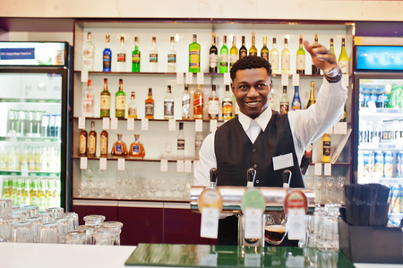 African american bartender at bar pouring from tap fresh beer into the glass in pub.の写真素材