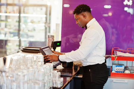 African american bartender wear on bow tie using cash terminal screen at bar.