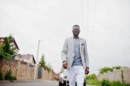 Rich and stylish african american man in blazer and white pants, eyeglasses posed against suv car.の写真素材