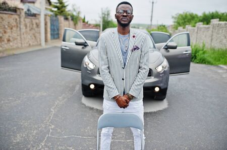 Rich and stylish african american man in blazer and white pants, eyeglasses posed against suv car.の写真素材