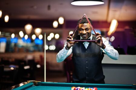 Young handsome african man wearing white shirt, black vest and bow tie play pool billiard.の素材 [FY310127071033]