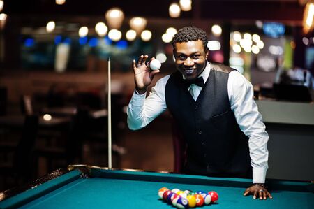 Young handsome african man wearing white shirt, black vest and bow tie play pool billiard.の写真素材