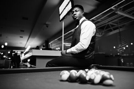 Young handsome african man wearing white shirt, black vest and bow tie play pool billiard.
