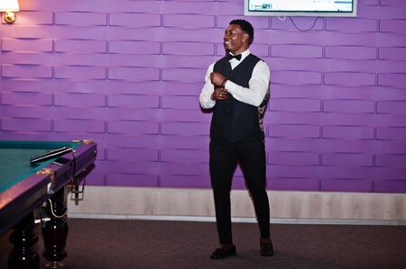Young handsome african man wearing white shirt, black vest and bow tie standing against pool...