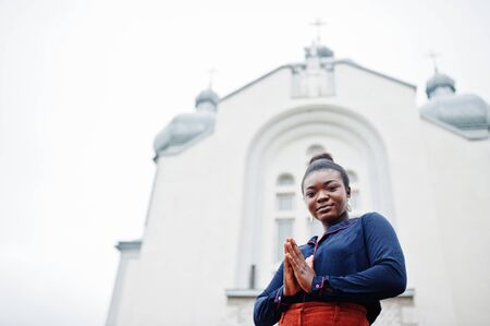 African woman in orange pants and blue shirt posed against large church. Faith and believe on God.の写真素材
