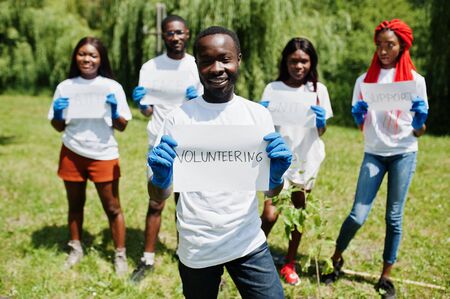 Group of happy african volunteers hold blank board with volunteering sign in park. Africa volunteering, charity, people and ecology concept.の写真素材