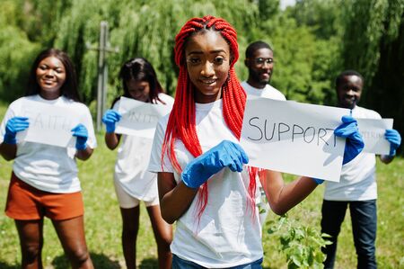 Group of happy african volunteers hold blank board with support sign in park. Africa volunteering, charity, people and ecology concept.の写真素材