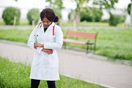 Young african american female doctor in white coat with a stethoscope posed outdoor.の写真素材