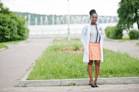 Young african american female doctor in white coat with a stethoscope posed outdoor.の写真素材