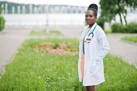 Young african american female doctor in white coat with a stethoscope posed outdoor.の写真素材