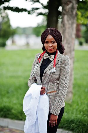 Young african american female doctor hold white coat on hand with a stethoscope posed outdoor.の写真素材