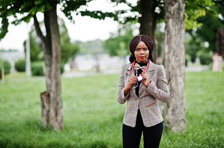 Young african american female doctor hold white coat on hand with a stethoscope posed outdoor.