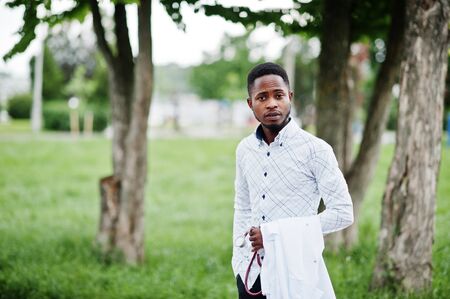 Young african american male doctor hold white coat on hand with a stethoscope posed outdoor.の写真素材