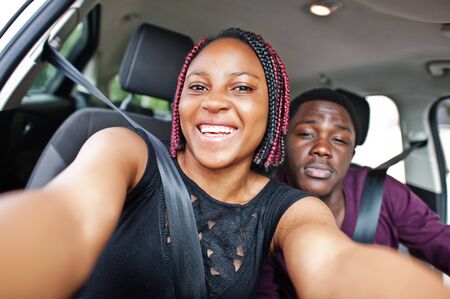Beautiful young african american couple sitting on the front passenger seats while handsome man driving a car. Making selfie together.の写真素材