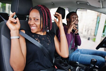 Beautiful young african american couple sitting on the front passenger seats while handsome man driving a car. Listening music and dance.の写真素材