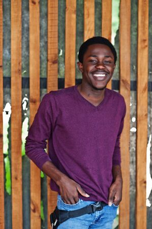 Young african american man in violet jumper posed against wooden wall.