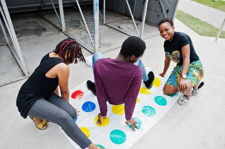 Group of three african american friends play twister game outdoor.