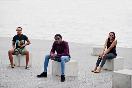 Three african american friends sitting on stone cubes outdoor.の写真素材
