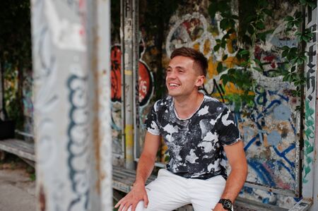 Lifestyle portrait of handsome man posing on the street of city with graffiti wall.
