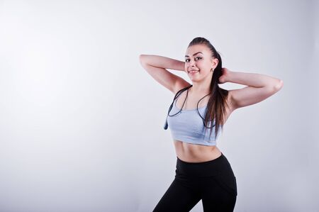 Cheerful attractive young fitness woman in top and black leggings with jump rope isolated over white...