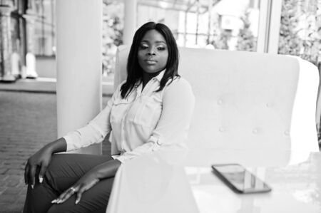 Formally dressed african american business woman in white blouse and red trousers sitting on outdoor...