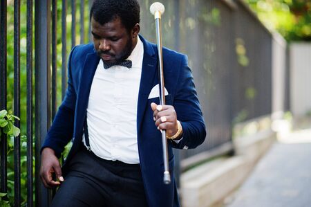 Handsome fashionable african american man in formal wear and bow tie with walking stick.の写真素材