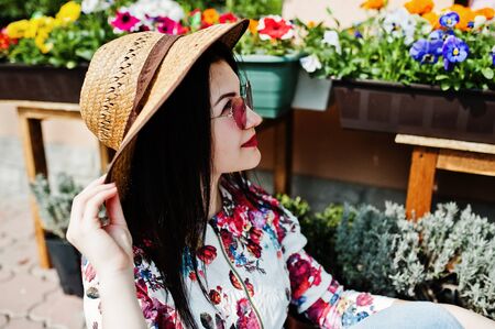 Summer portrait of brunette girl in pink glasses and hat against flowers shop.の写真素材