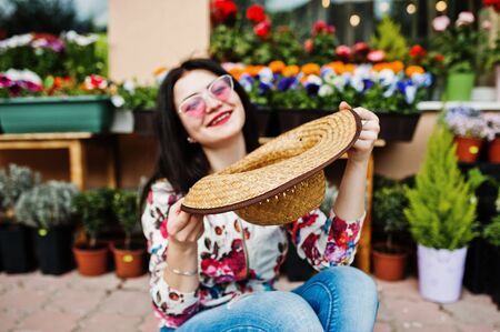 Summer portrait of brunette girl in pink glasses and hat against flowers shop.の写真素材