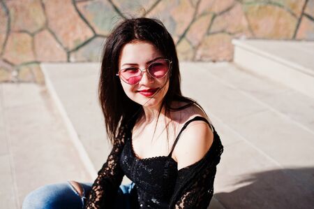 Portrait of brunette girl in pink glasses wear on black posed outdoor on sunny day.