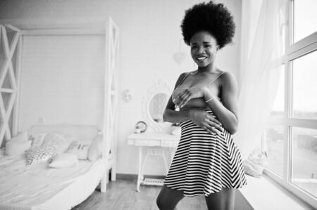 Attractive african american woman with afro hair wear on skirt pink top, posed at white room. Fashionable sexy black model.の写真素材