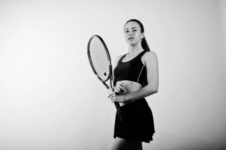 Black and white portrait of beautiful young woman player in sports clothes holding tennis racket while standing against whiteの写真素材
