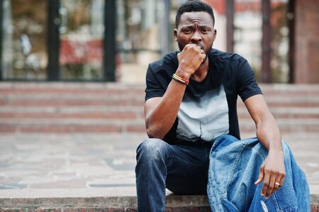 Young attractive serious african american man model. Modern handsome guy in jeans jacket sitting on...