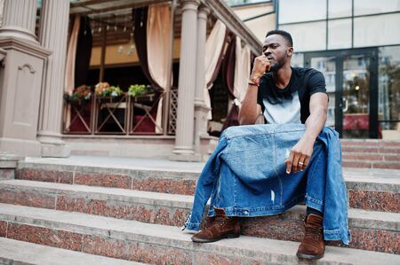Young attractive serious african american man model. Modern handsome guy in jeans jacket sitting on...