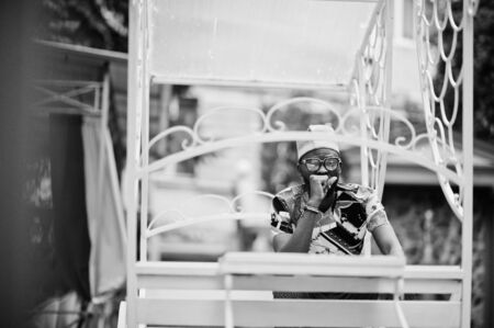 Handsome afro american man wearing traditional clothes, cap and eyeglasses sitting at white...