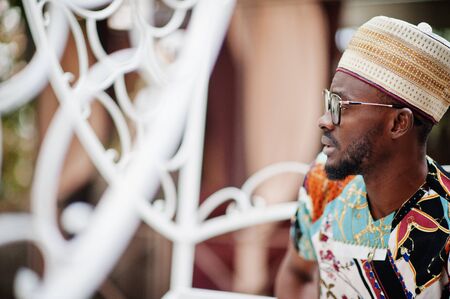 Handsome afro american man wearing traditional clothes, cap and eyeglasses sitting at white carriage.の写真素材