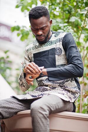 Handsome afro american man wearing traditional clothes in modern city looking at his watches.