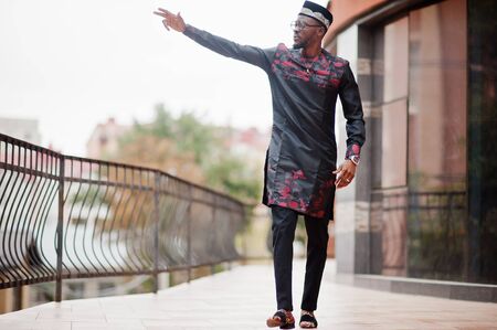 Handsome afro american man wearing traditional clothes, cap and eyeglasses in modern city raised his hand.の写真素材